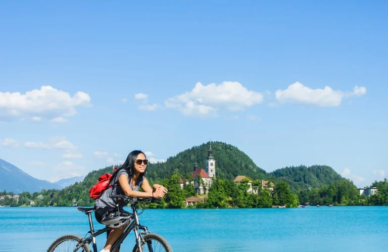 Asiatisk turist på cykel med smuk udsigt over Bled-søen med kirke på ø i Slovenien, Europa